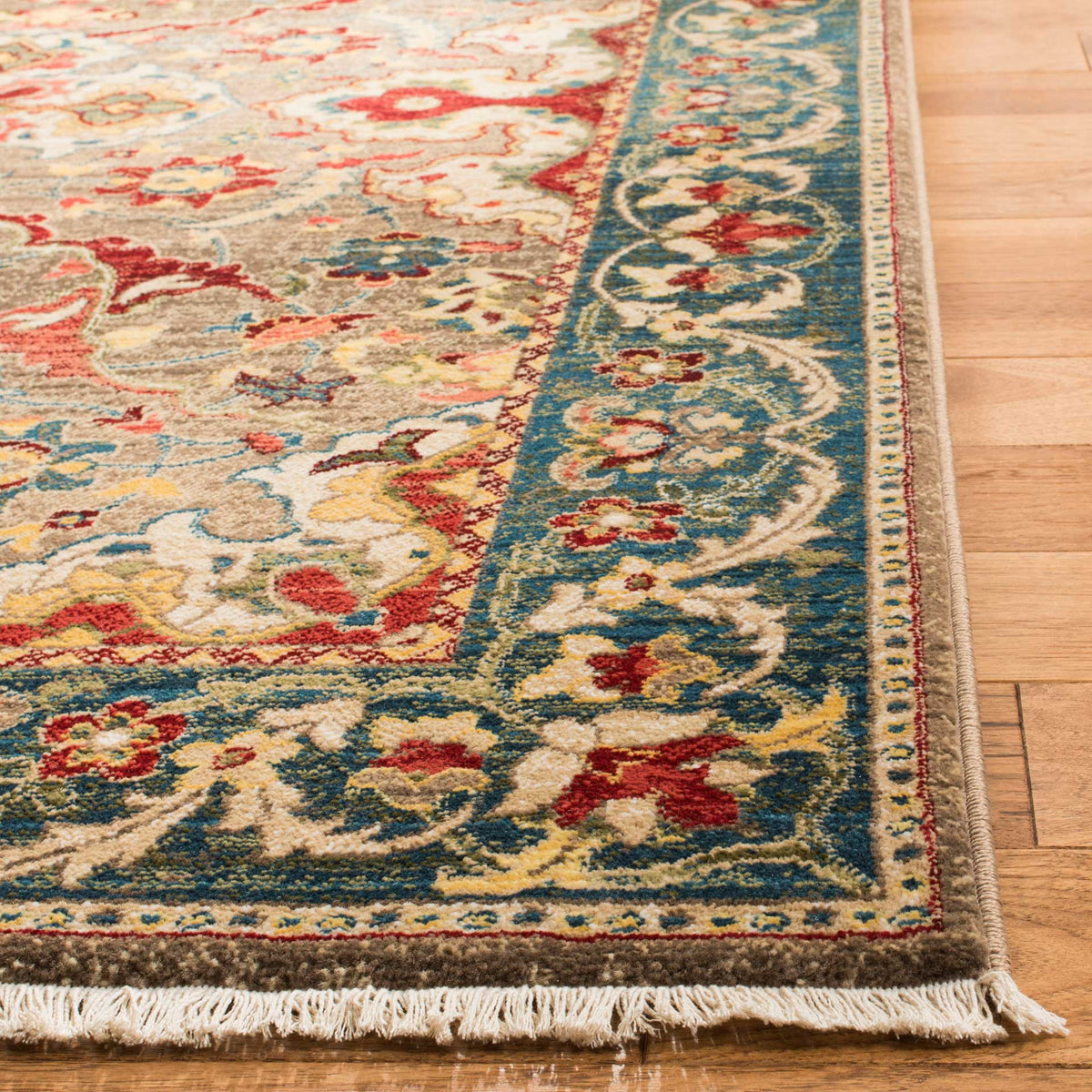 Blue floral scrollwork frames the taupe field, with red accents and ivory fringe at the edge.