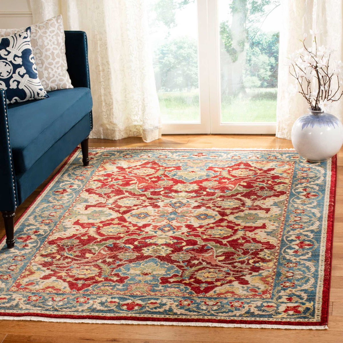 A vivid red floral rug with a blue border adds traditional detail to a bright living room.