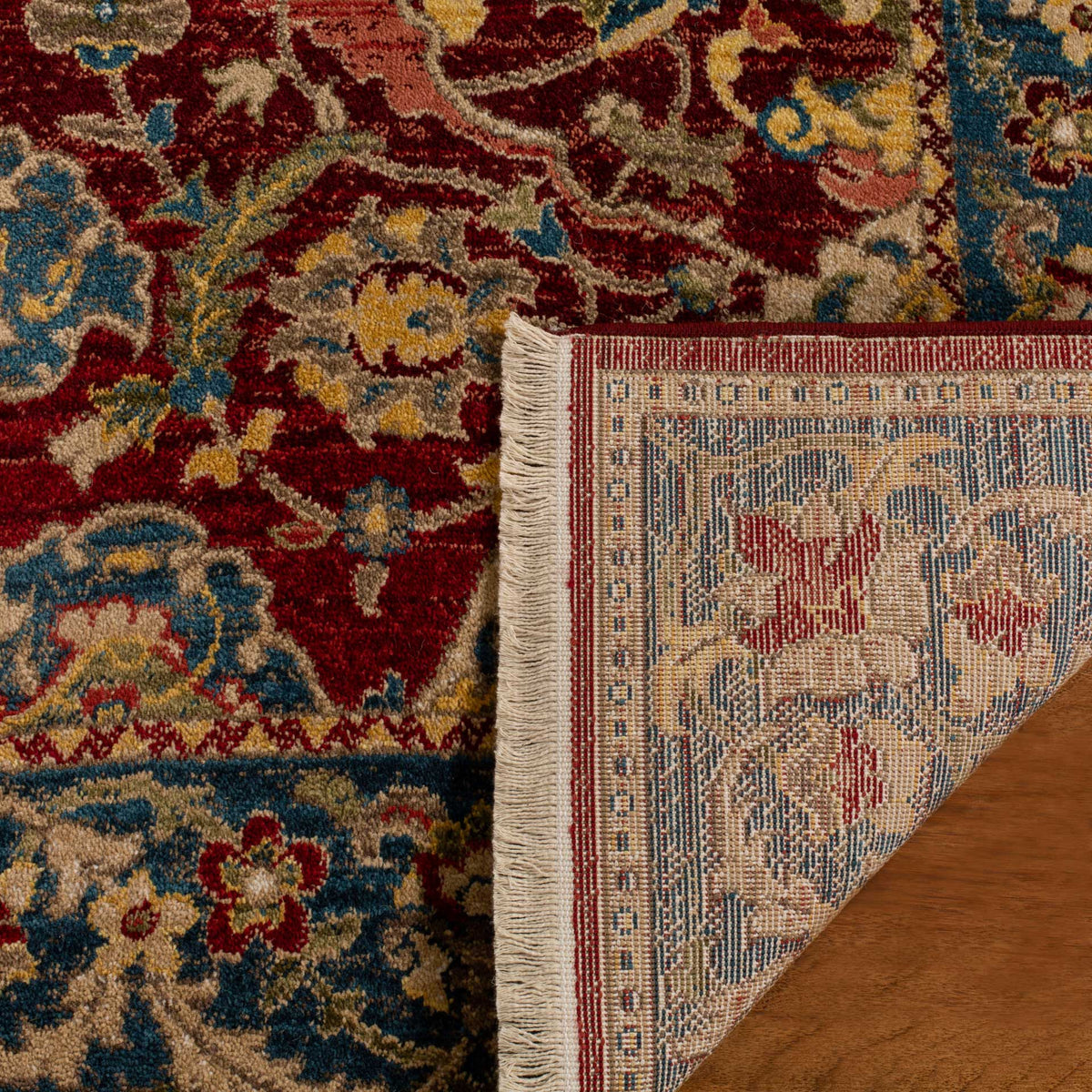 A patterned woven backing sits beneath the rug's red floral pile and blue border.