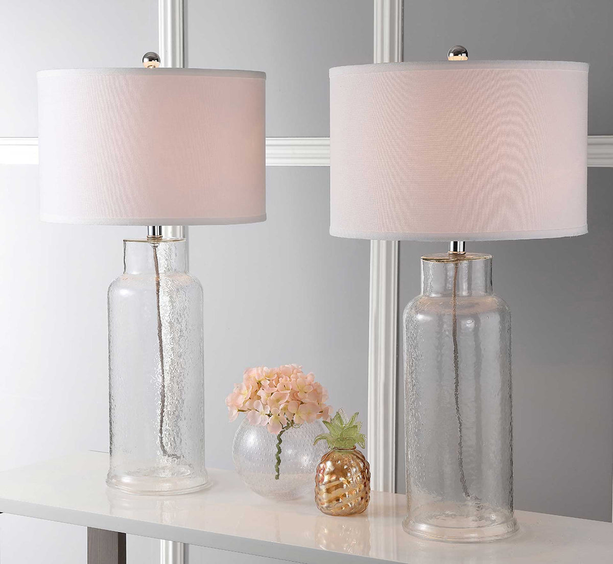 Two clear glass bottle lamps glow softly beneath white drum shades