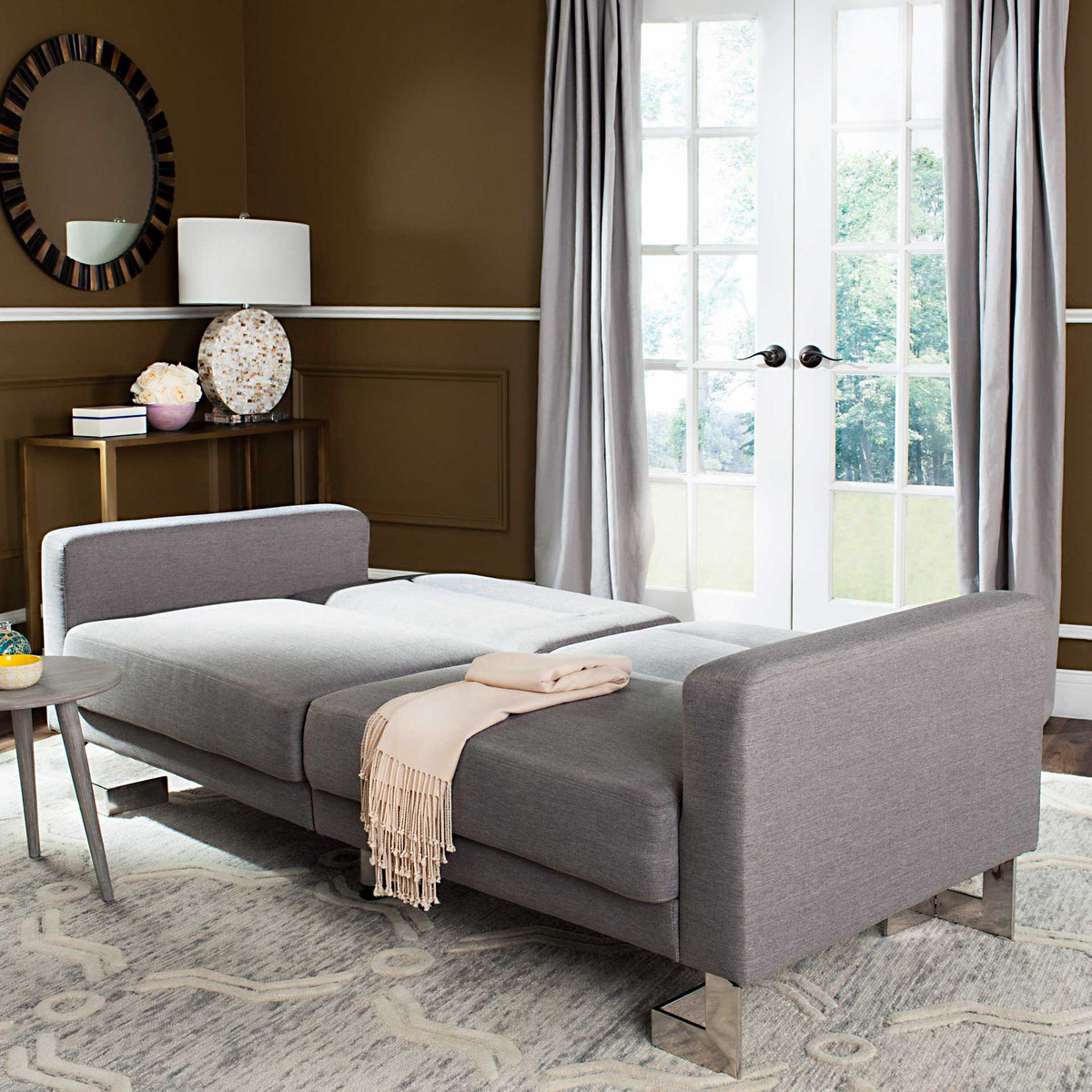 Gray upholstery forms a generously padded bed with squared armrests and sleek silver-tone feet.