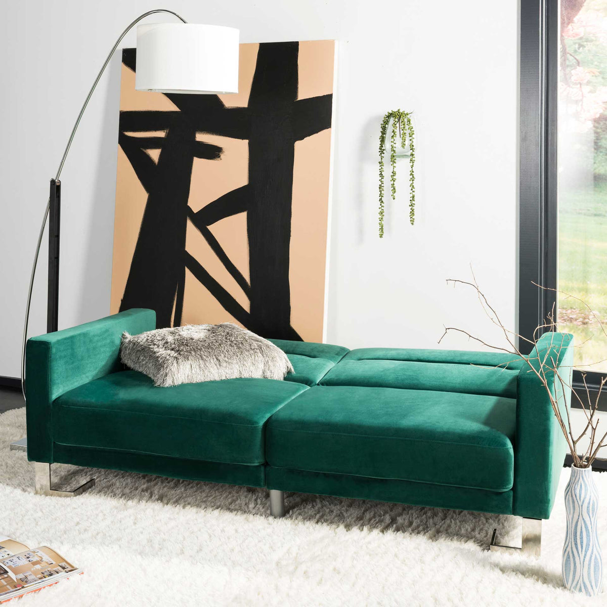 Emerald velvet cushions create a broad, padded bed with clean-lined arms and metallic feet.