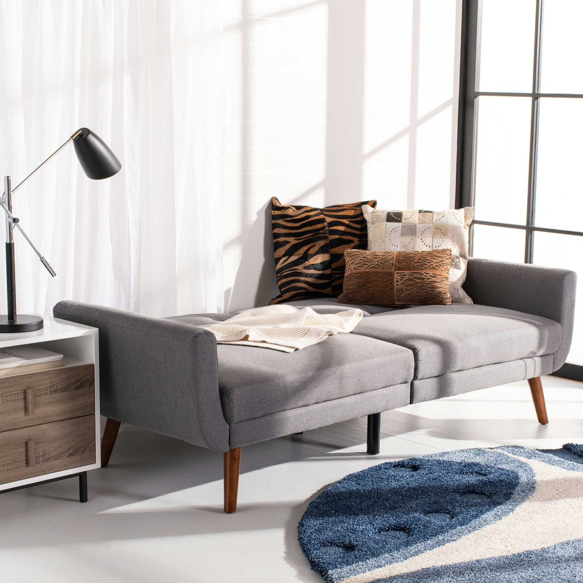 Stone gray futon unfolds into a cushioned bed with soft fabric and warm wood legs.