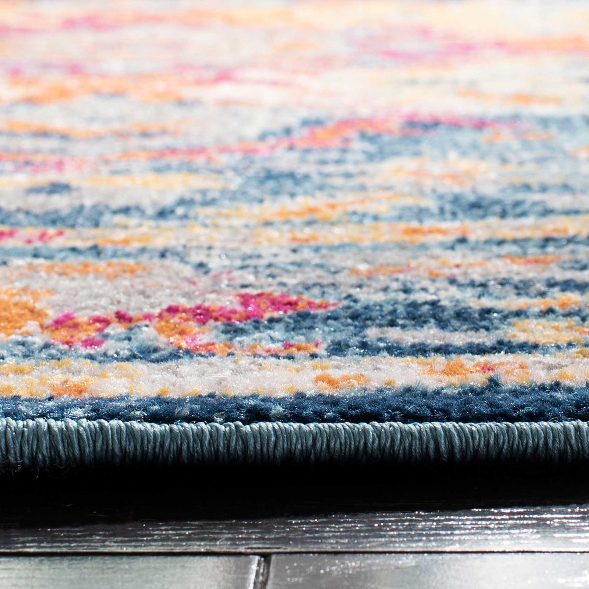 A neatly bound edge finishes the textured teal pile with flecks of fuchsia, orange, and gold