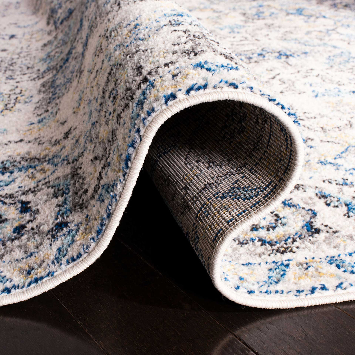 A folded edge reveals the woven backing beneath blue and ivory patterned pile