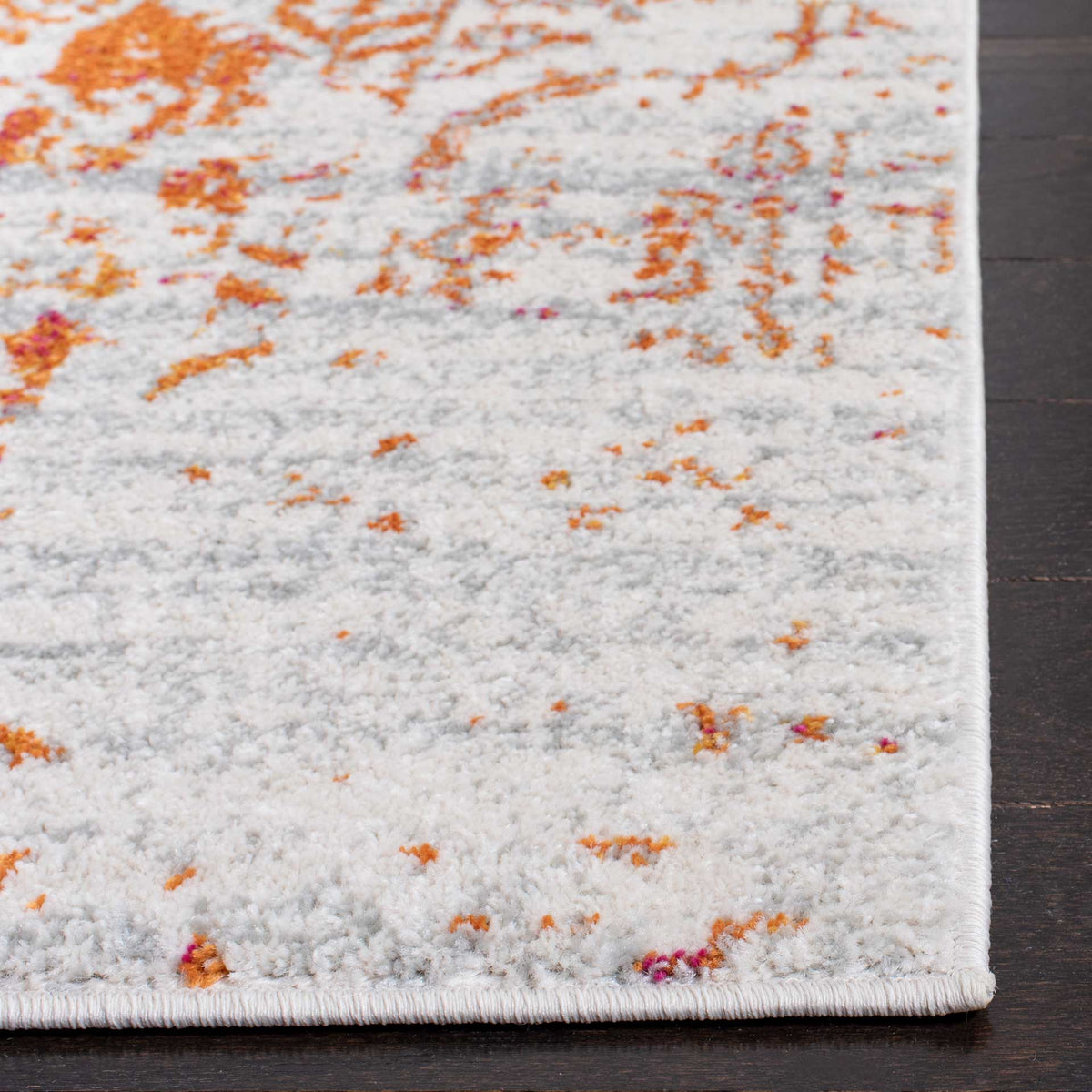 Scattered orange accents fleck the ivory pile beside a neatly bound rug corner