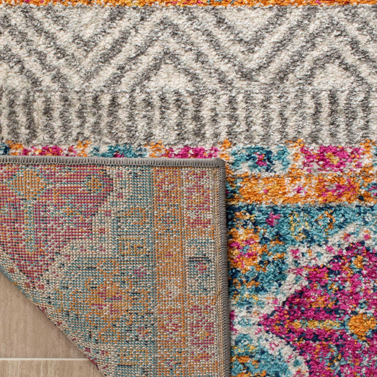 A folded edge reveals woven backing beneath colorful motifs and gray diamond patterns.