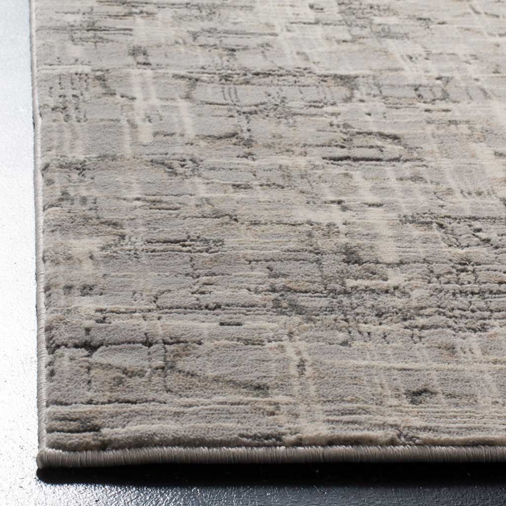 A neatly bound edge frames the rug's soft gray pile and weathered abstract pattern