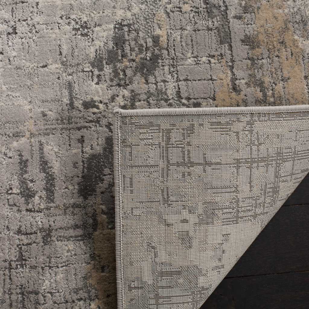 A folded corner reveals the rug's woven backing beneath its gray abstract pile.