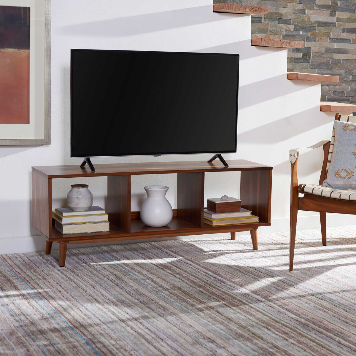Three open cubbies organize books and accents beneath a TV on this low wood media stand