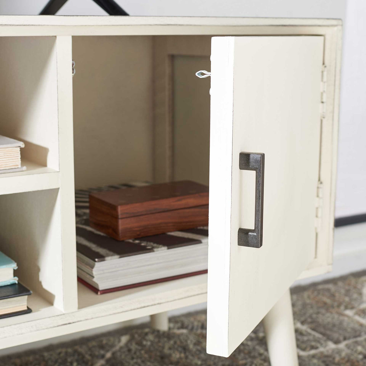A white cabinet door opens to enclosed storage for books and living room essentials.