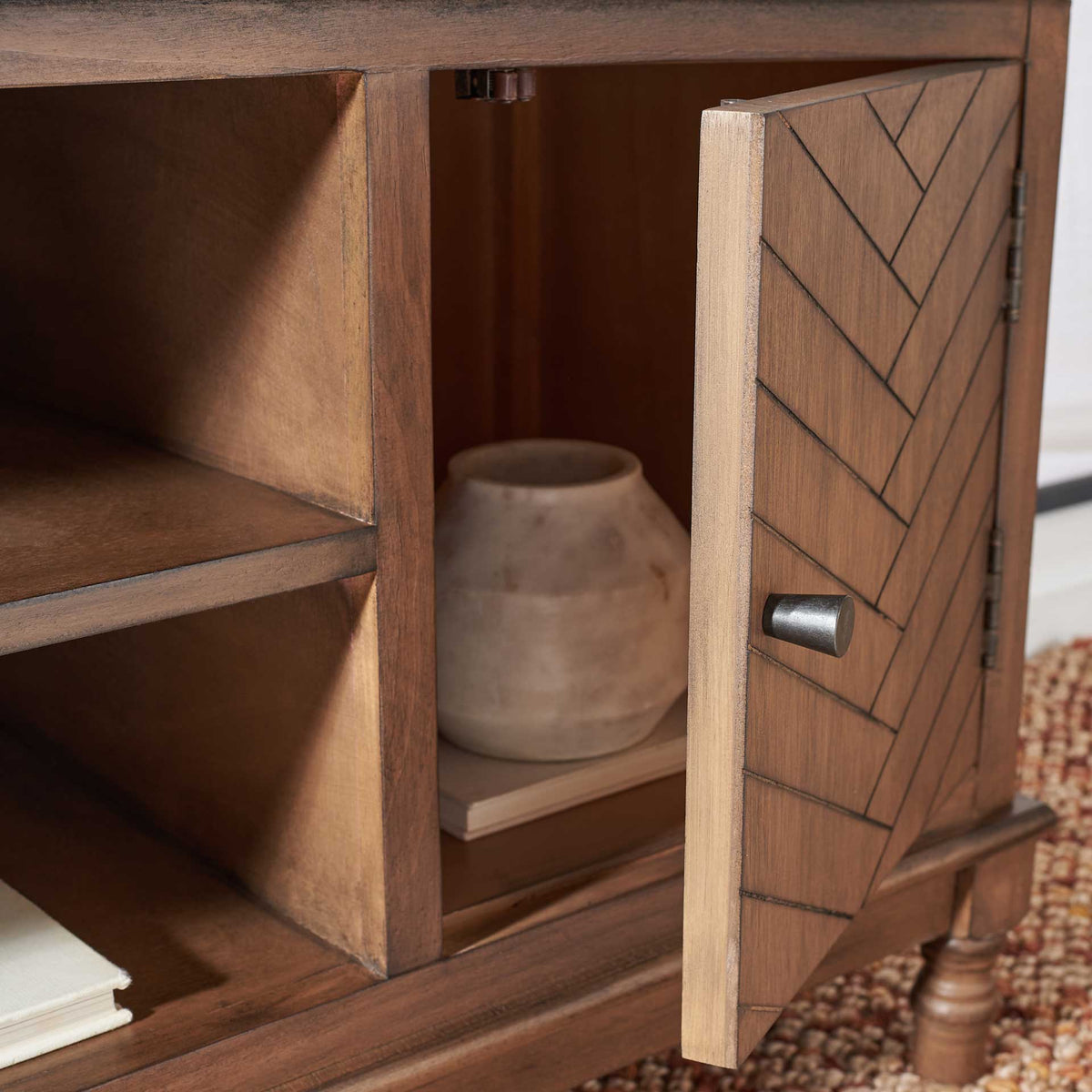 The open herringbone door reveals a cabinet holding a ceramic vessel beside spacious shelves.