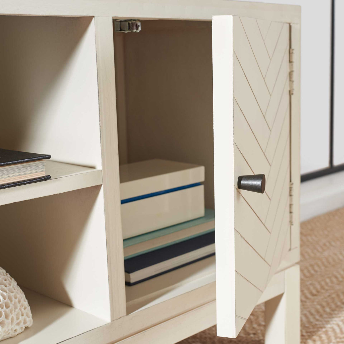 An open white chevron door reveals cabinet storage beside shelves for books and decor.