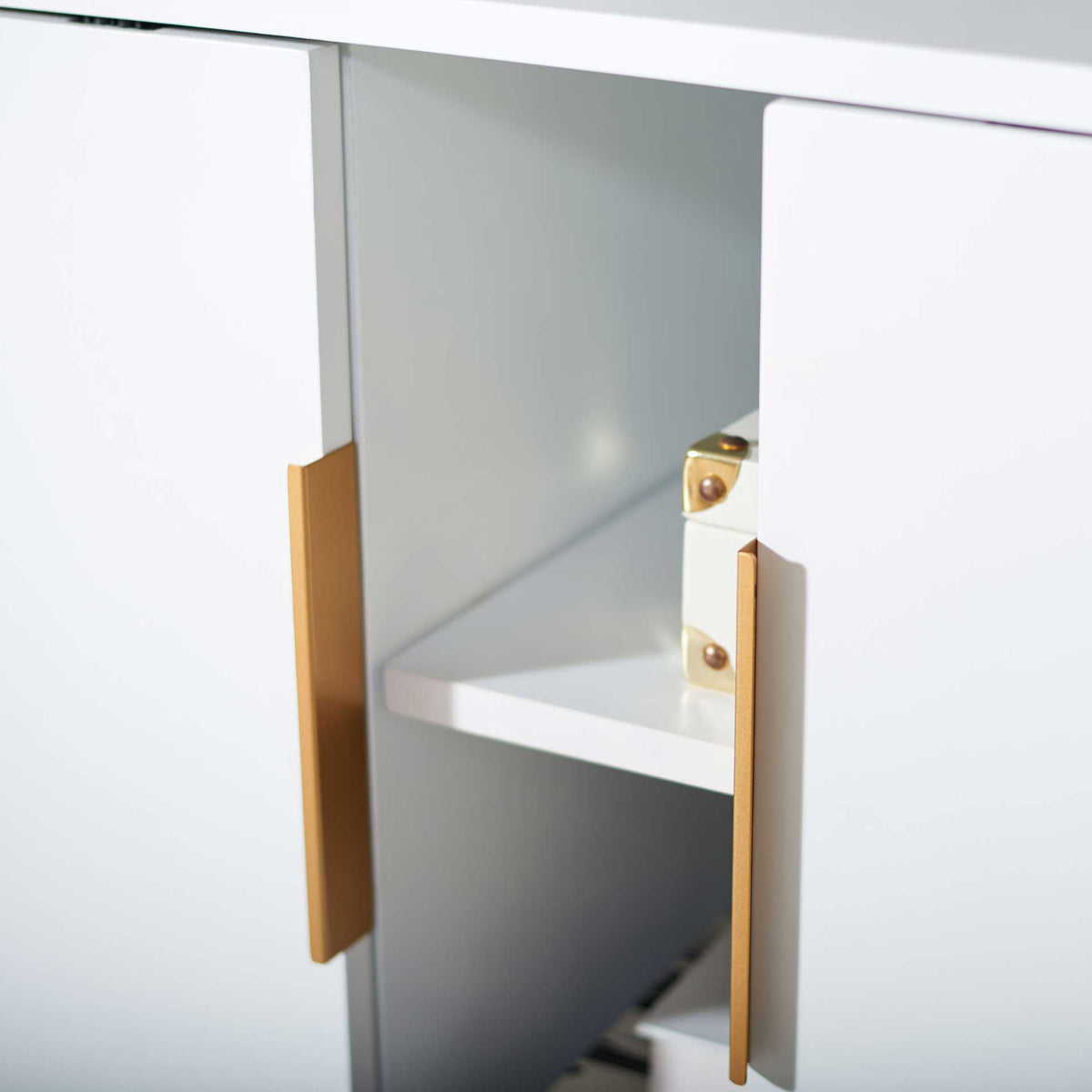 An accessible center shelf sits between smooth white doors with slim gold pulls.