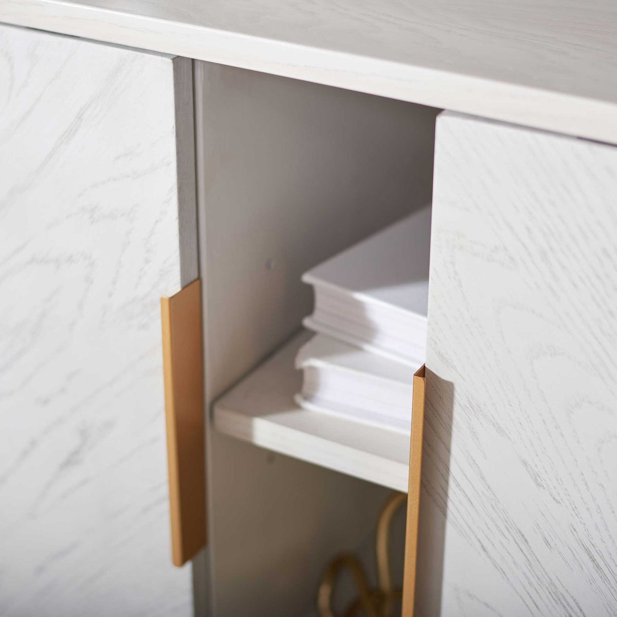 Whitewashed doors and slim gold pulls frame an open shelf holding books and accessories.