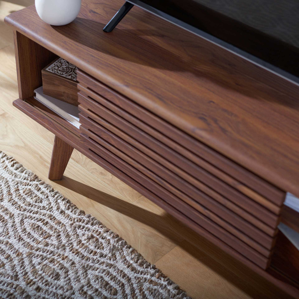 A slatted sliding door and smooth wood-grain top pair with an open cubby for books and decor.