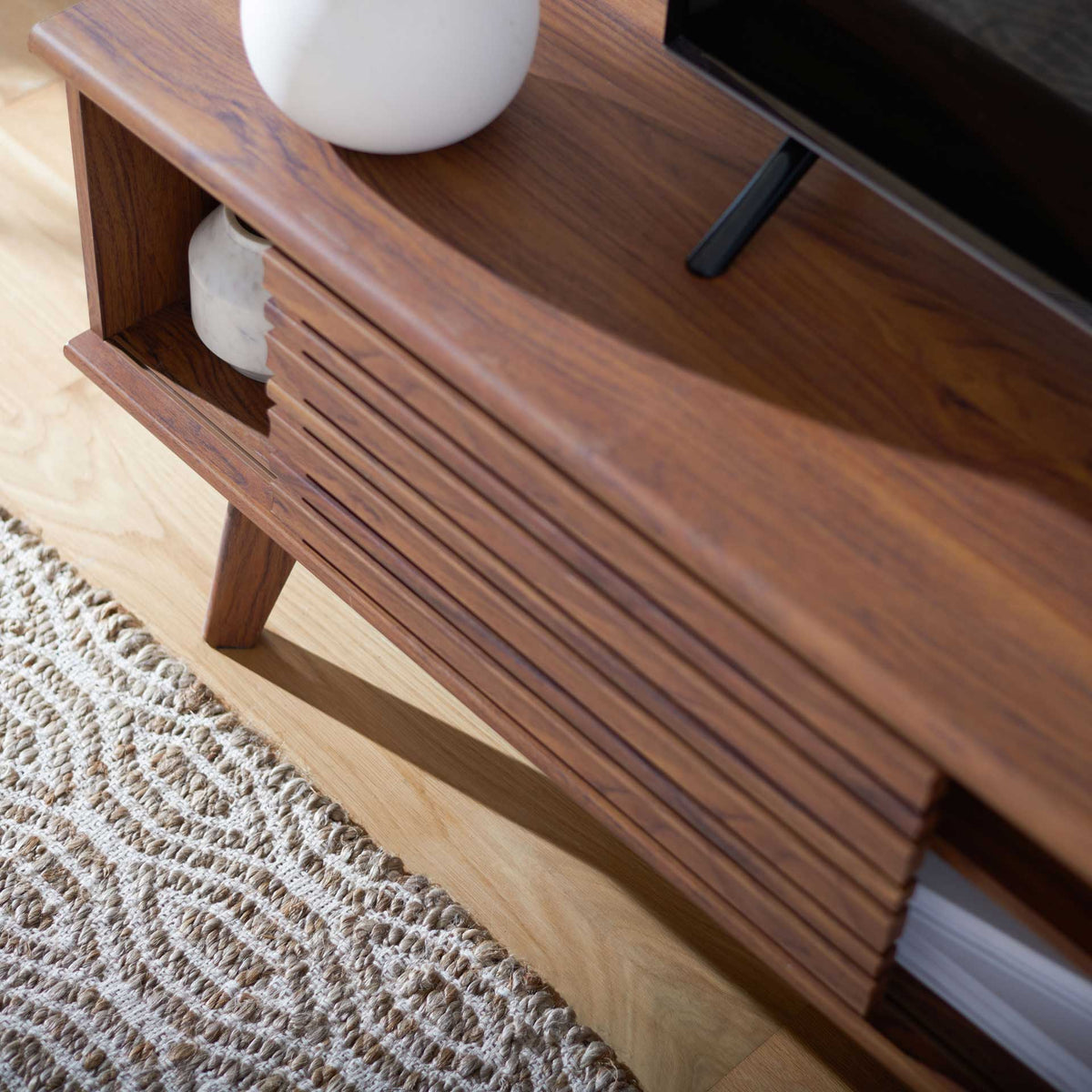 Sliding slatted doors reveal side compartments for books and decor beneath the TV-ready top.