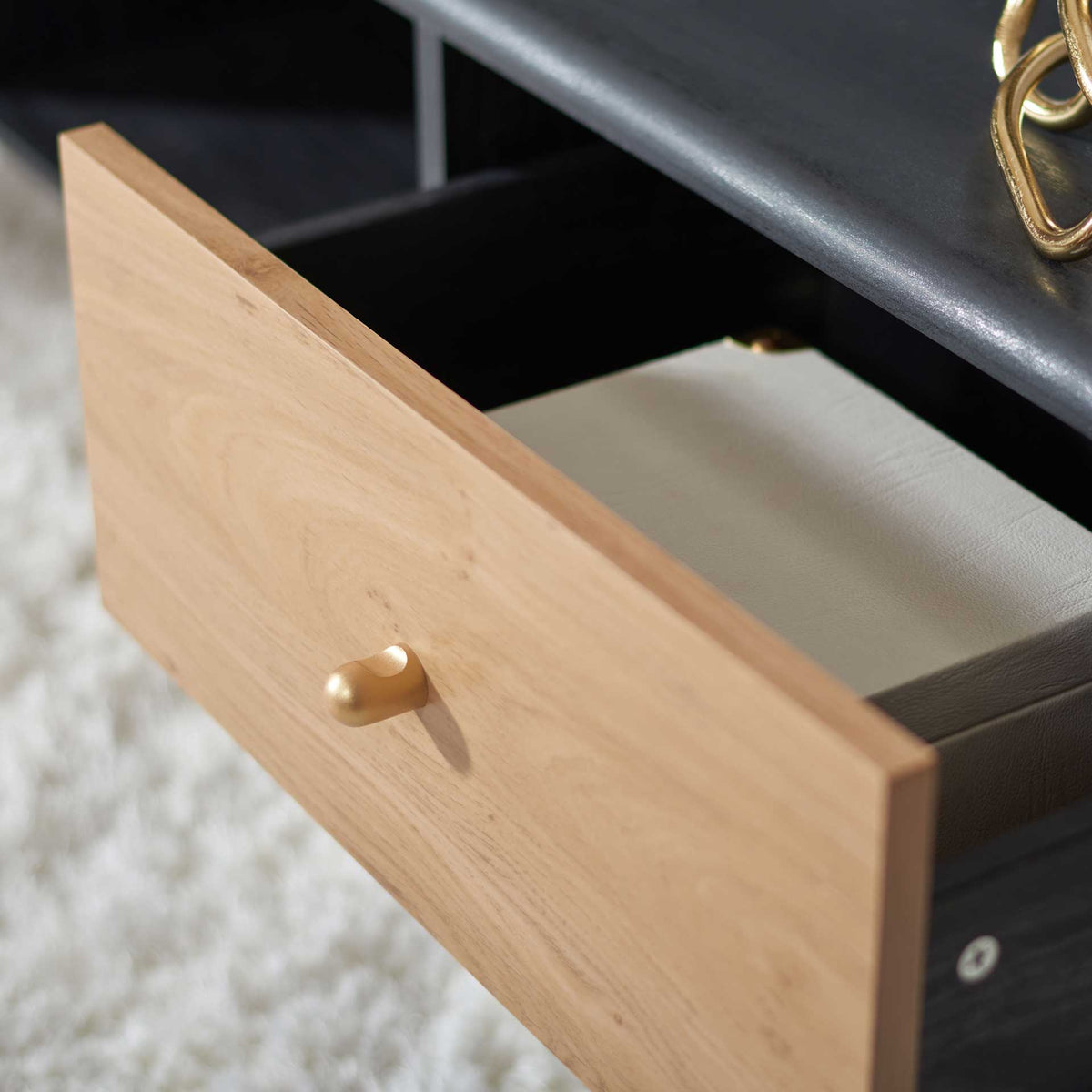 A gold-tone pull opens the wood-grain drawer to reveal storage for books and living room essentials.