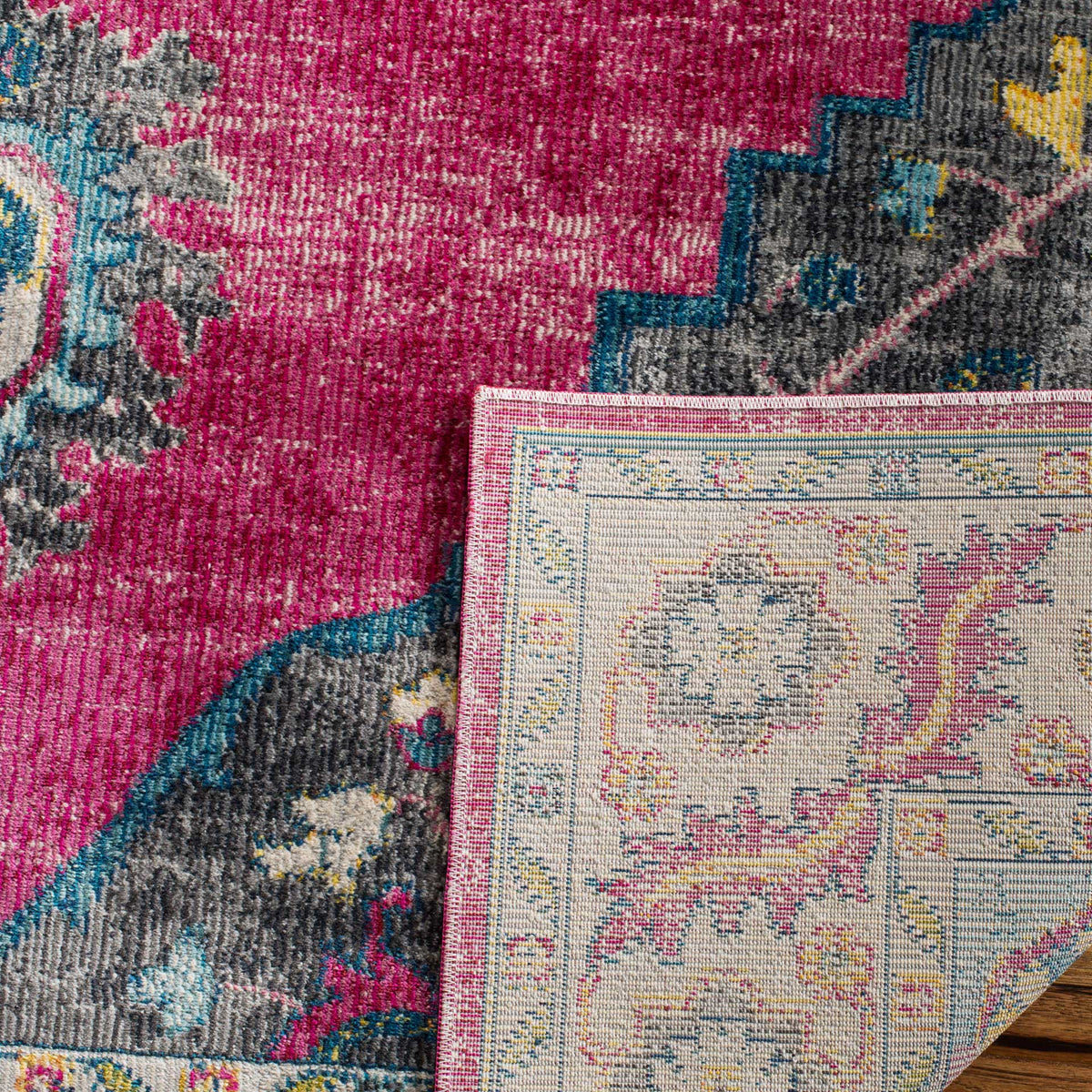 Folded fuchsia rug reveals a pale woven underside with subtle floral motifs beside its vibrant patterned pile