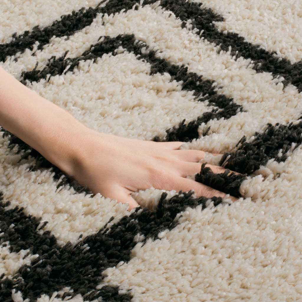 Thick cream-and-charcoal shag pile cushions a hand beneath its diamond pattern