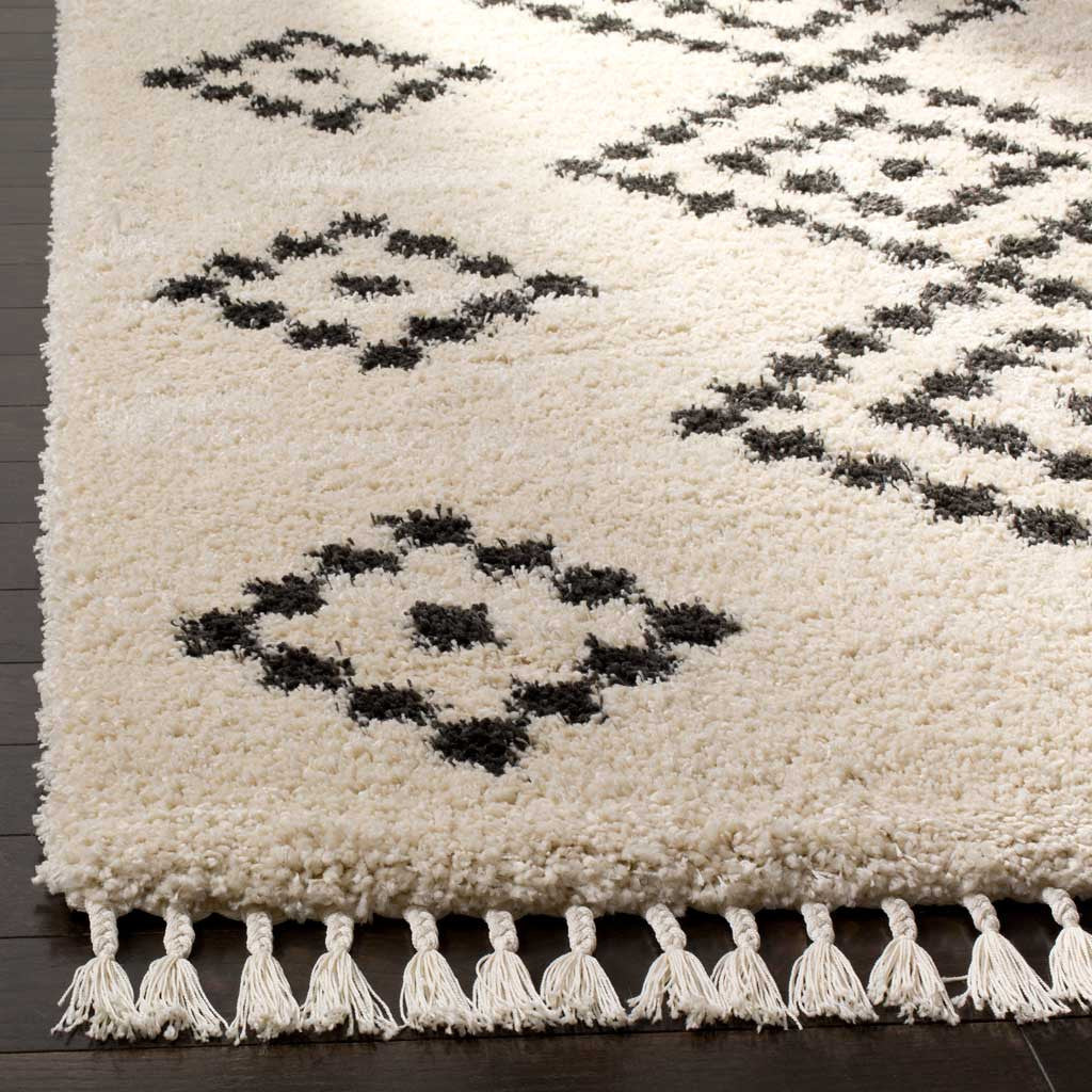 Thick cream pile frames charcoal motifs above a row of knotted tassels