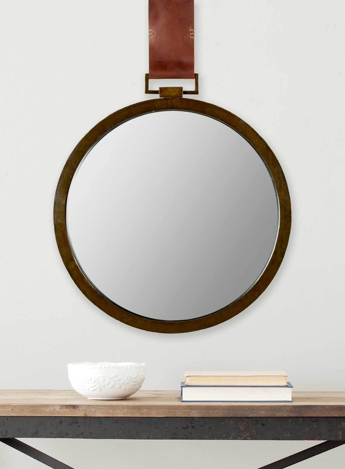 A slim antiqued gold rim and brown leather strap give this circular mirror understated style