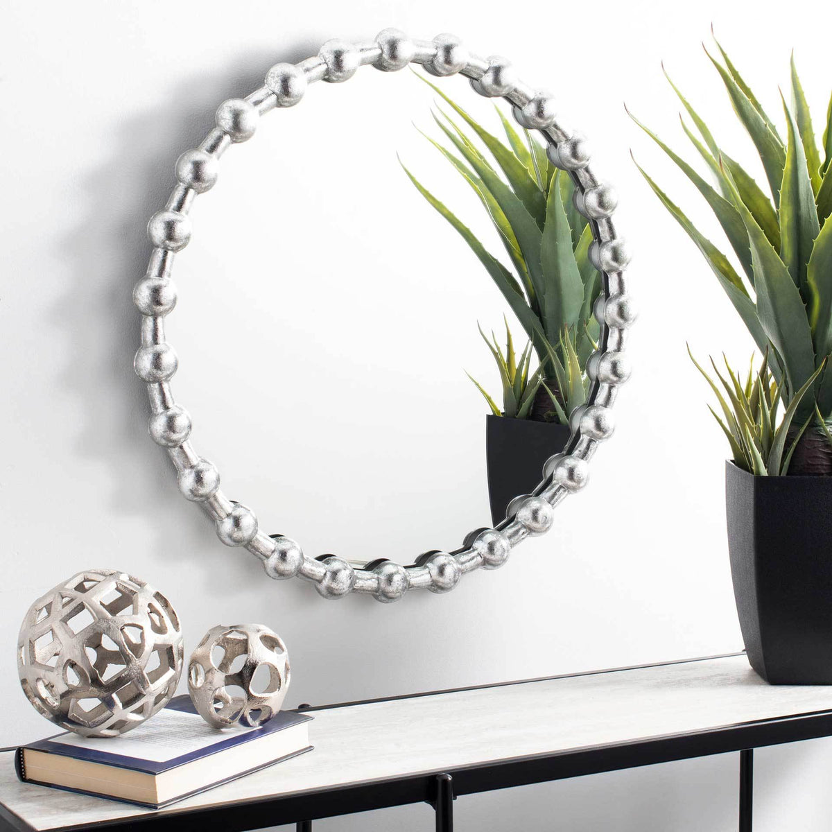 A silver-beaded mirror brings a luminous accent to the wall above a slim console.