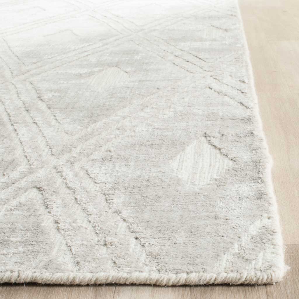 A neatly finished rug edge borders soft silver-gray pile and faint diamond lines