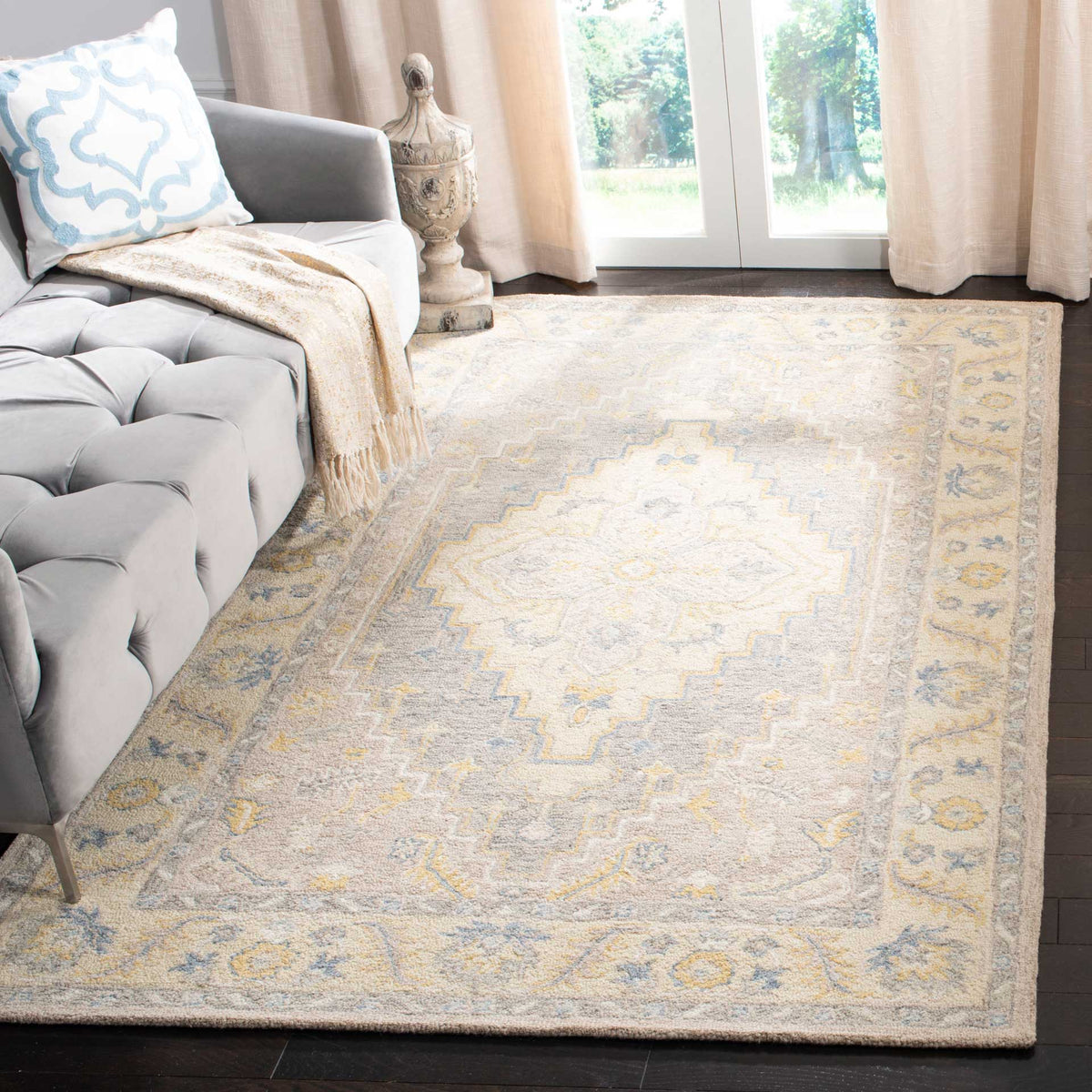 A muted floral medallion rug adds a warm, intricate foundation beside a tufted gray sofa.
