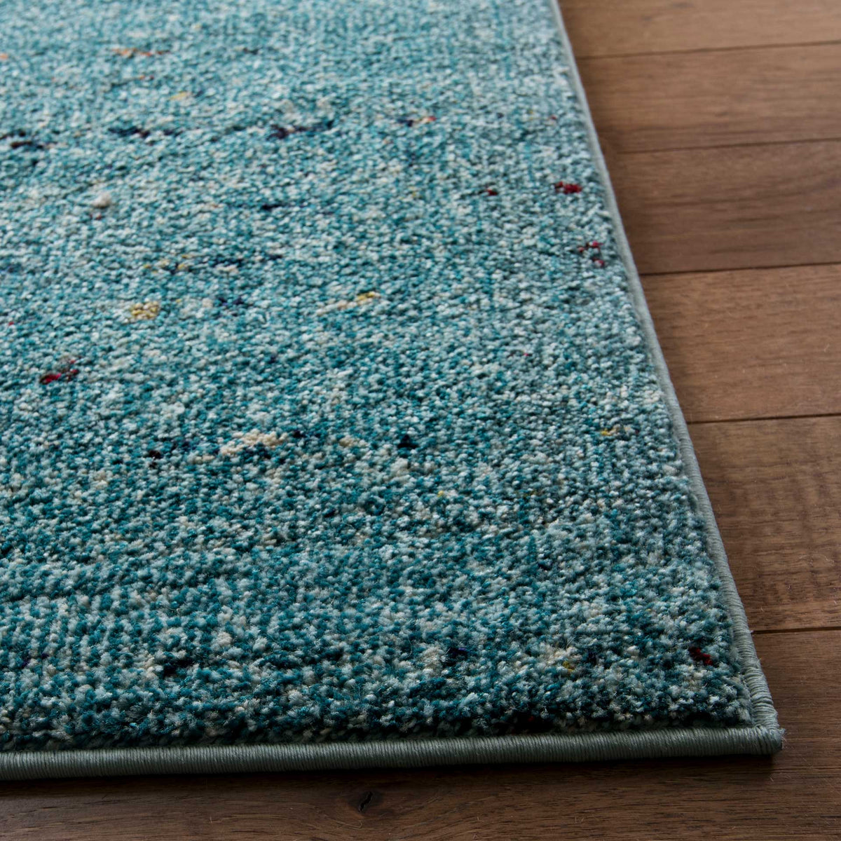 Bound rug corner highlights dense blue pile and subtle multicolored flecks