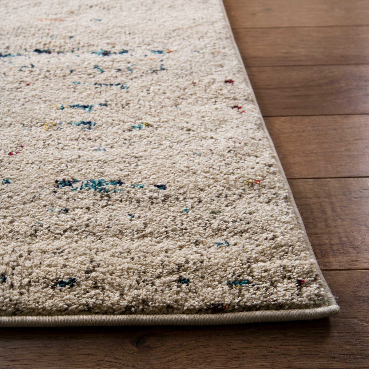 Bound ivory rug corner reveals textured pile with sparse blue and rust flecks