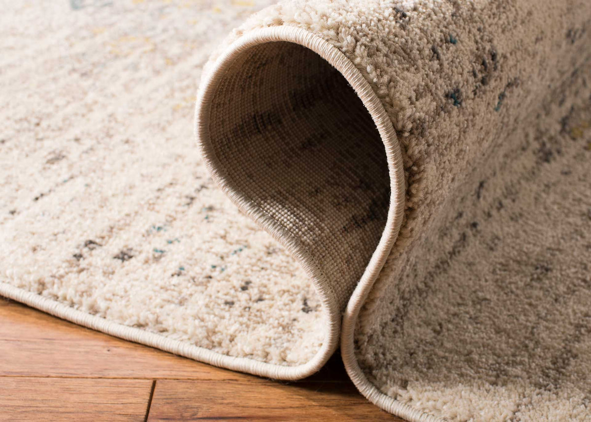 A curled edge reveals woven backing beneath softly textured ivory and gray pile