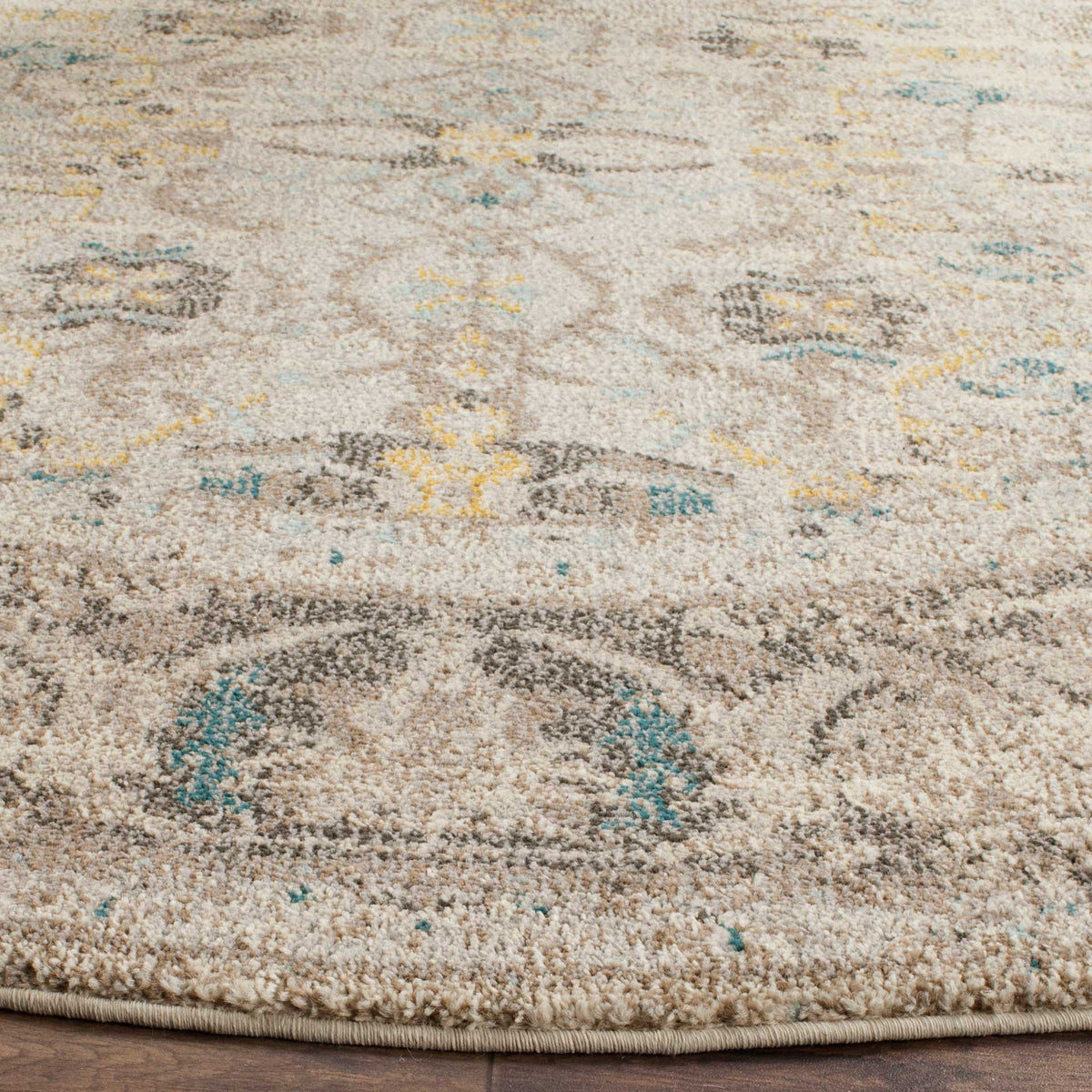 A neatly bound edge finishes the gray rug's textured teal, gold, and taupe floral pattern.