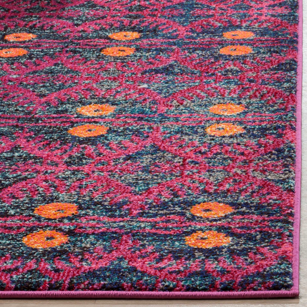 A neatly bound pink edge finishes a textured rug with pink scrolls and vibrant orange accents.