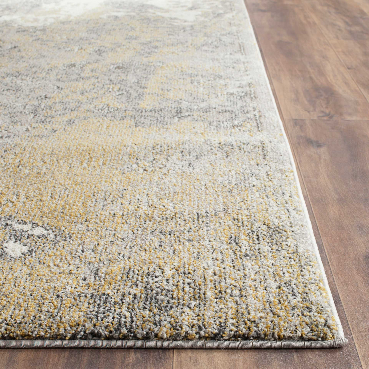 A neatly bound edge frames low, textured pile flecked with gold, ivory and gray.