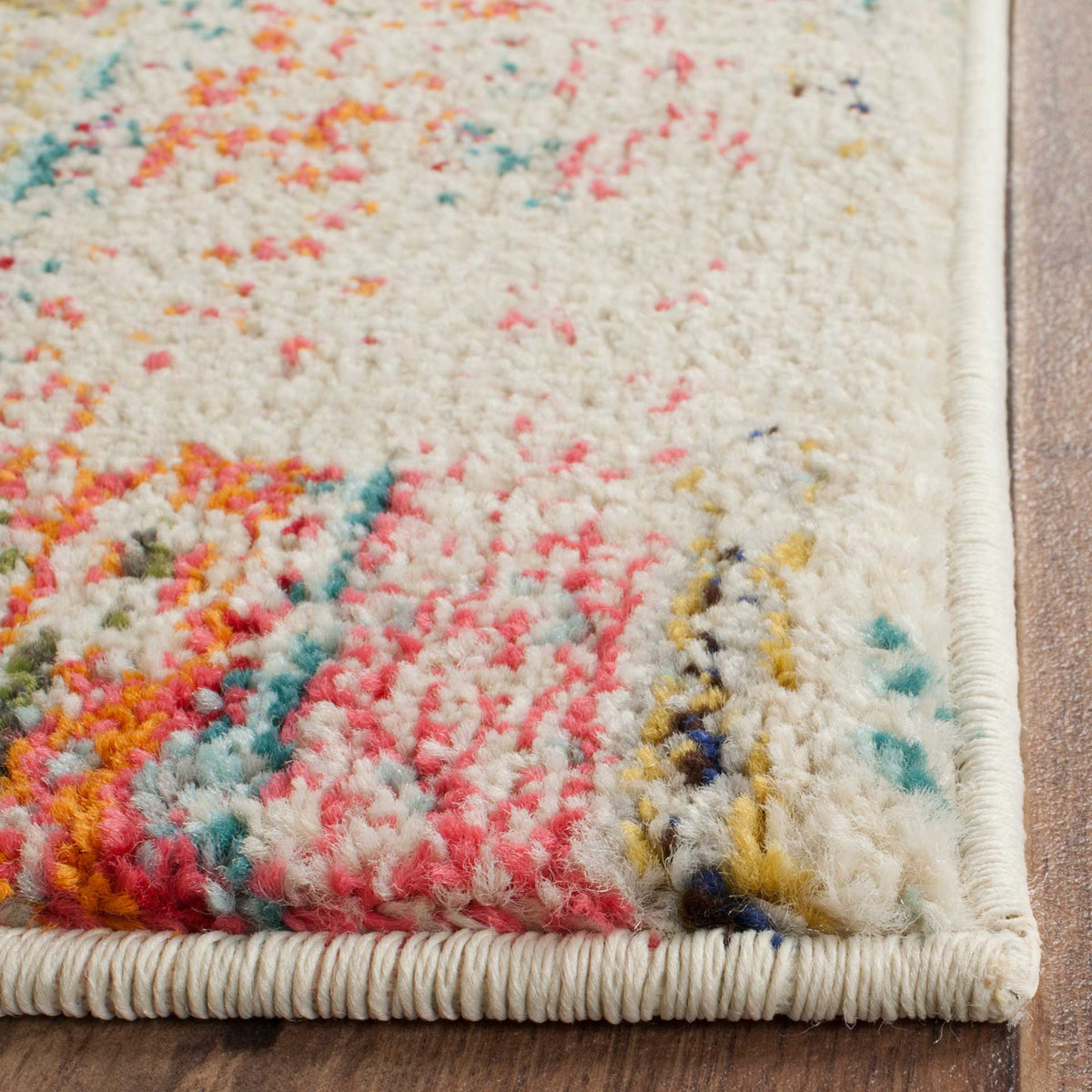 A bound edge frames textured cream rug pile with flecks of coral, teal, and gold.