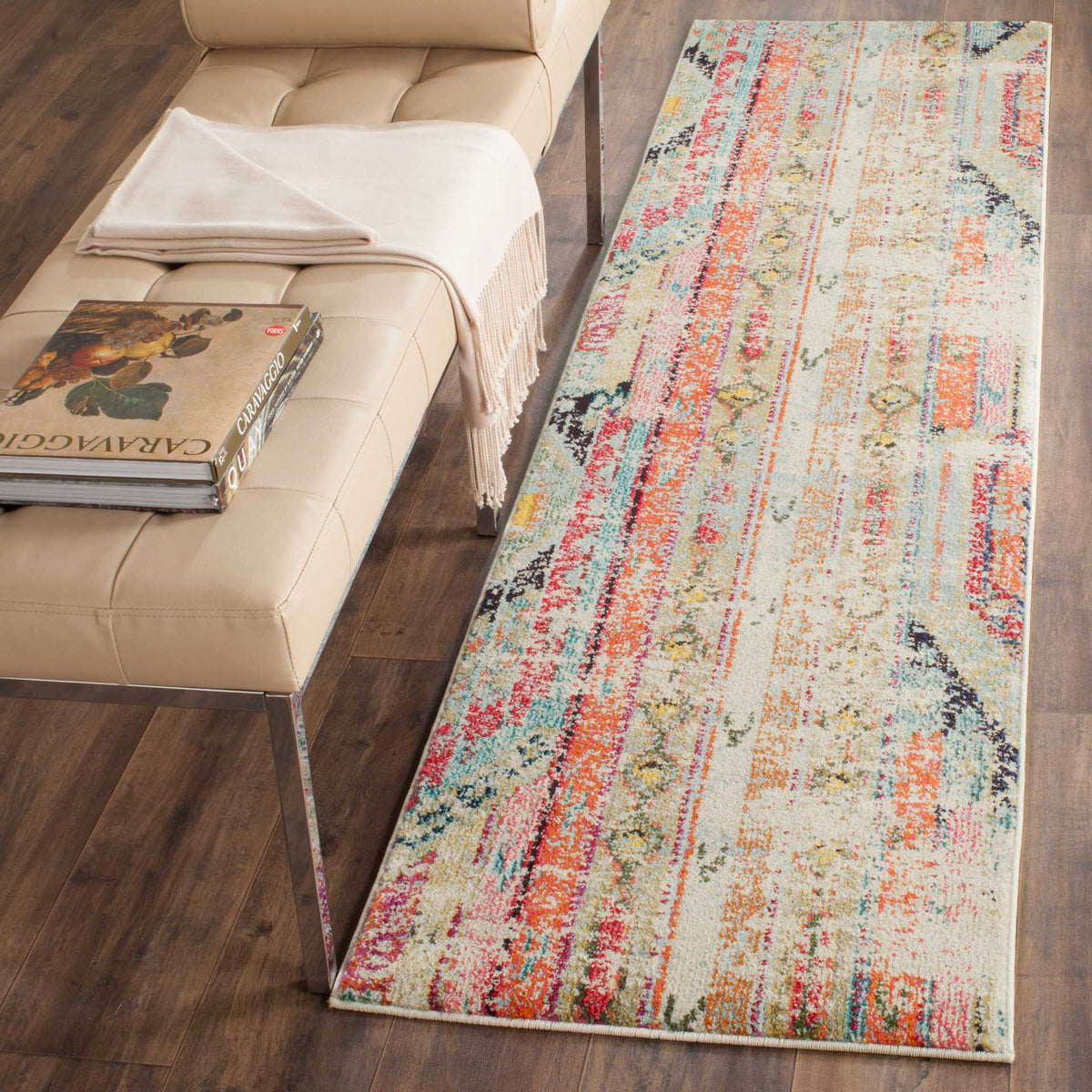 Long, narrow runner rug carries vibrant coral and teal motifs across a cream ground.