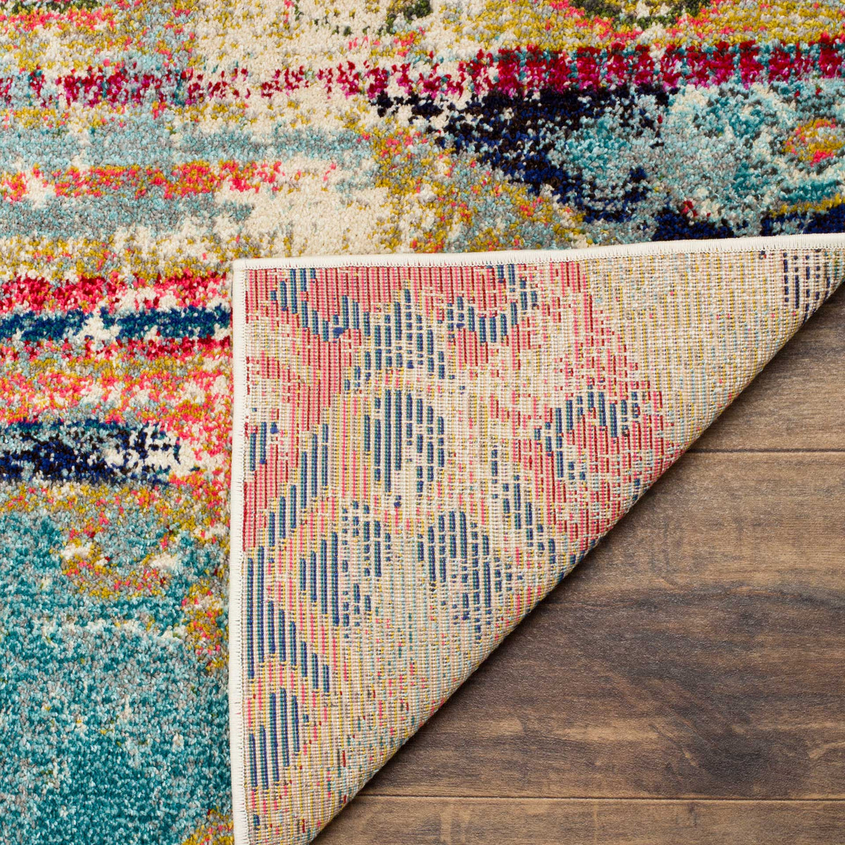 A folded edge reveals the rug's woven backing beneath aqua, coral, and cream patterns