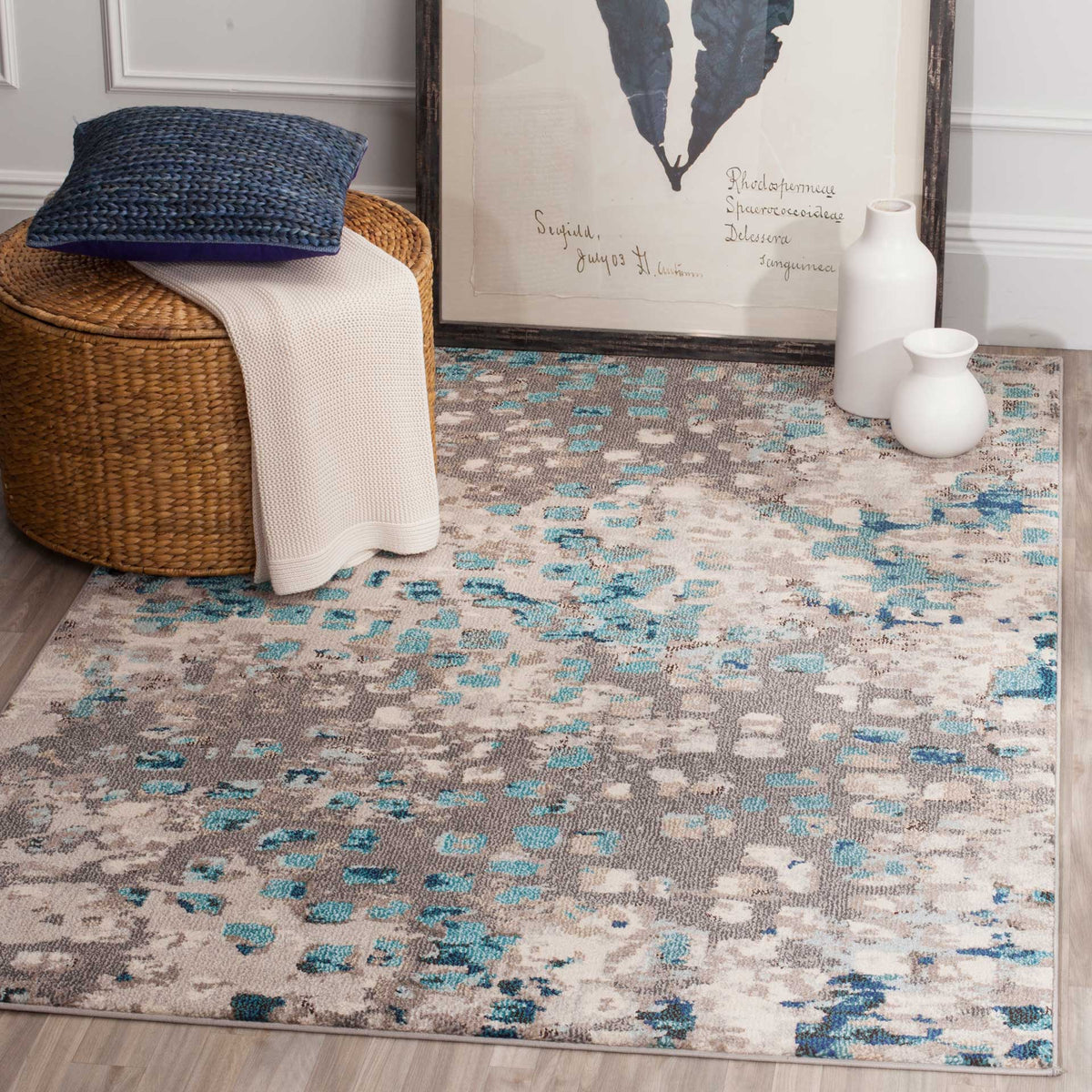 Gray and teal abstract rug complements a woven stool, cozy throw, and white vases