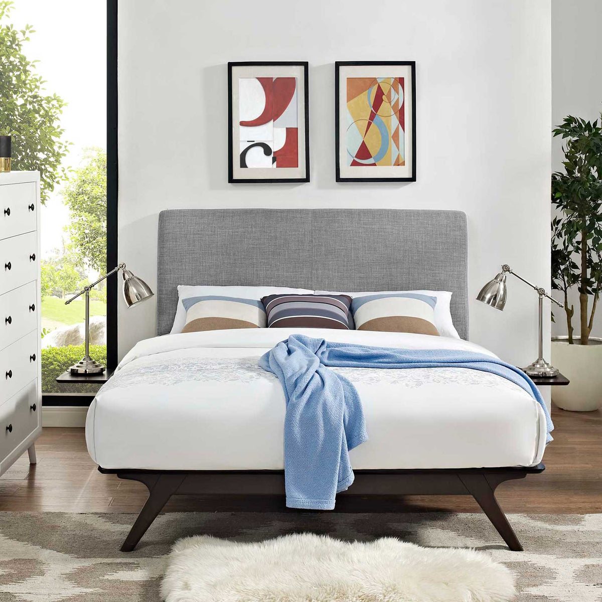 Gray upholstered headboard and dark tapered legs complement layered bedding and bedside tables