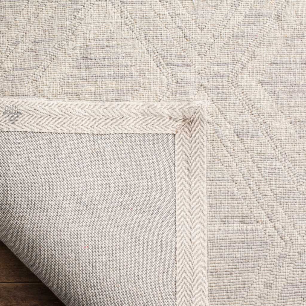A woven fabric backing and bound edges complement the silver and ivory rug's textured surface.