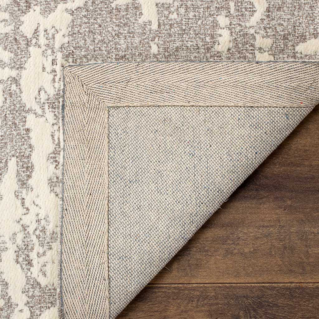 A woven underside and neatly bound corner complement the rug's light gray and ivory face.