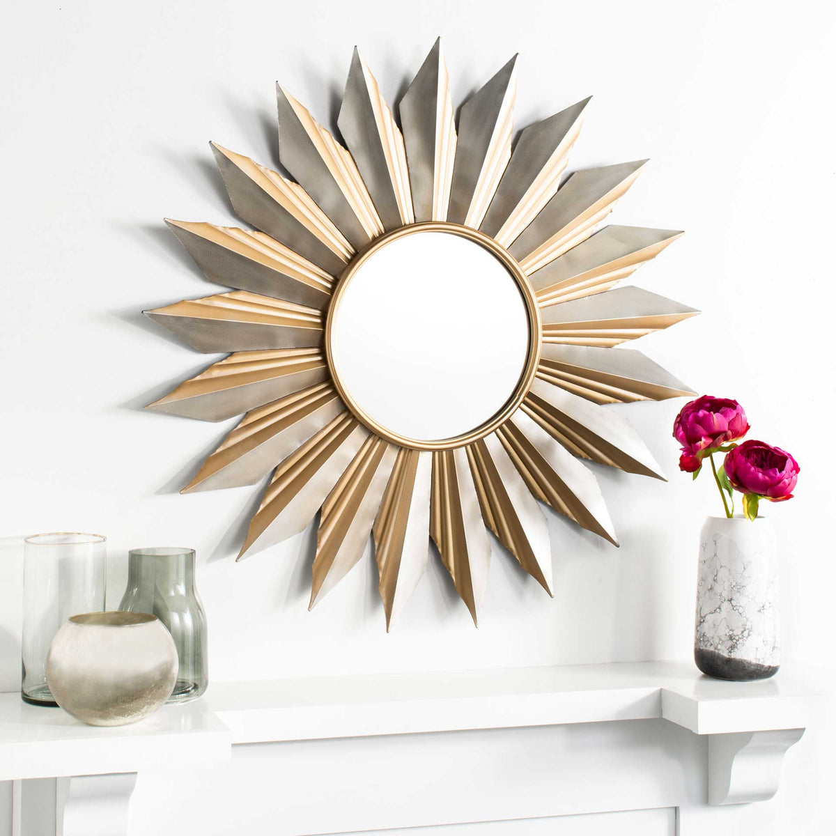A sculptural sunburst mirror brightens a mantel with its gold and silver-tone rays