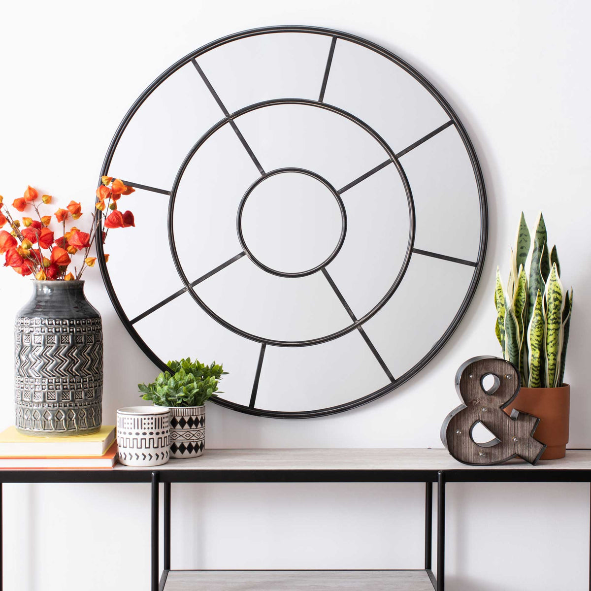An airy round mirror with dark radial framing adds geometric depth above a slim console table