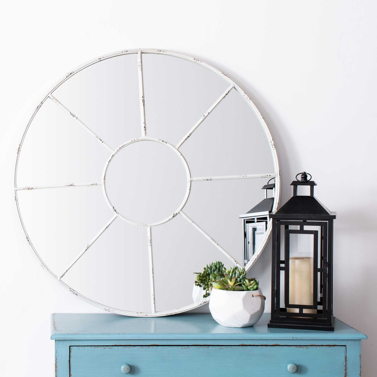 Distressed white spokes lend a round mirror an airy presence above a blue cabinet