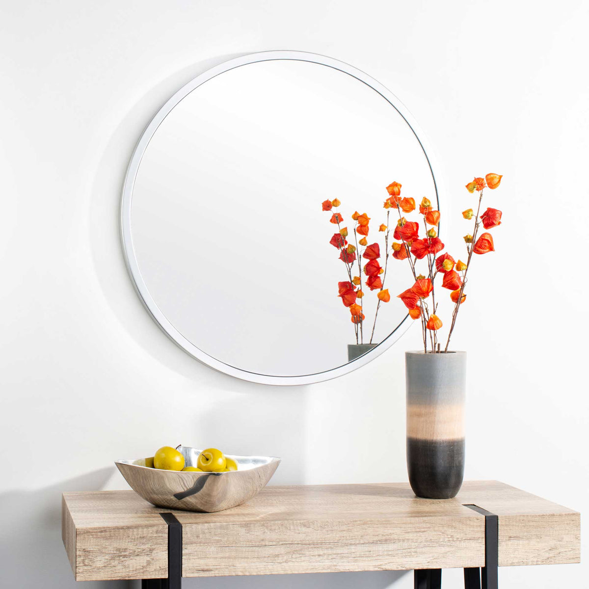 Silver-framed round mirror brings a bright finish above a natural wood console.