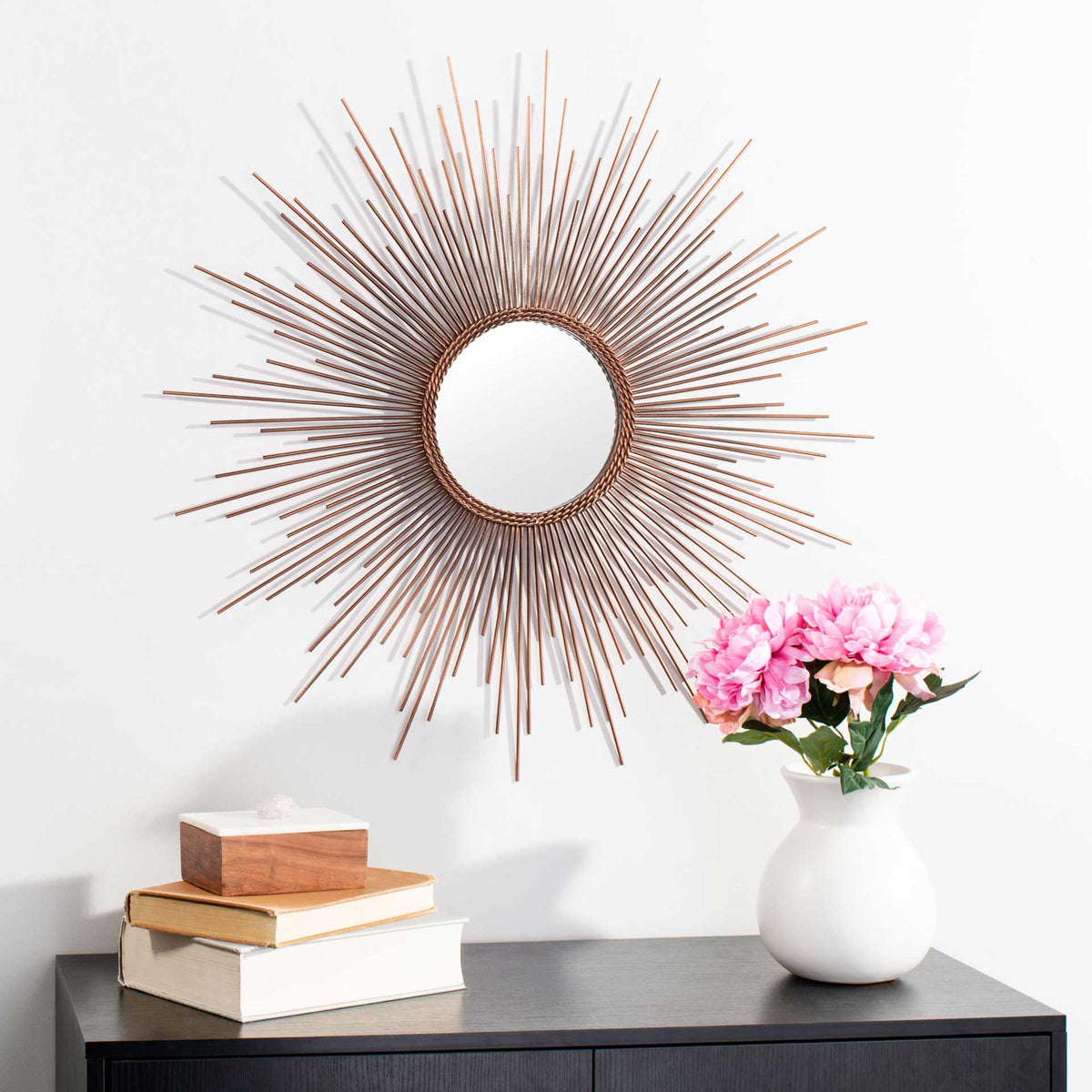 A round mirror with copper-toned sunburst rays adds warmth above a dark console