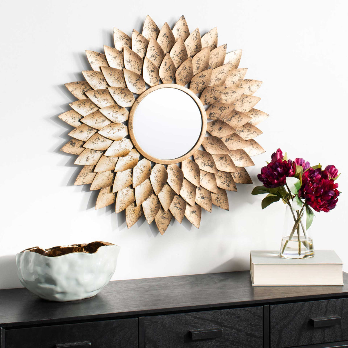 Gold leaf sunburst mirror adds sculptural warmth above a dark cabinet