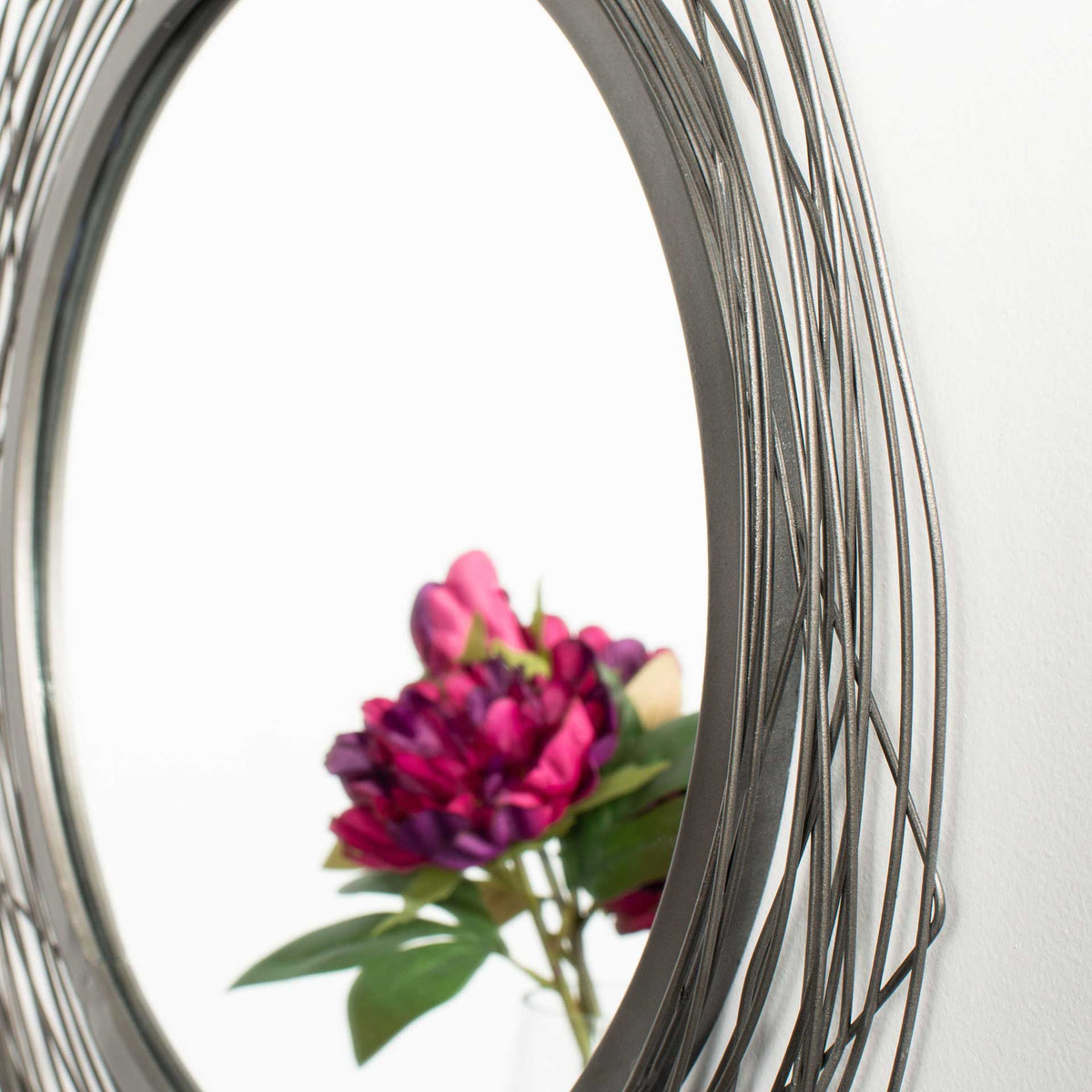 Layered black wire loops and a slim inner rim frame the mirror's floral reflection