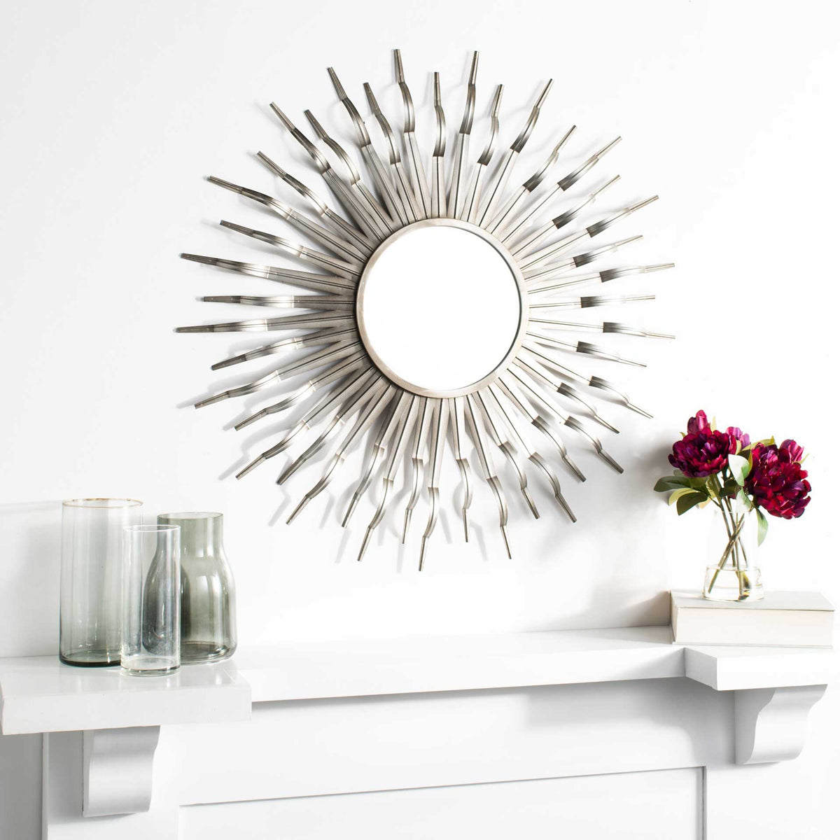 Gunmetal sunburst mirror creates a sculptural metallic focal point above a white mantel